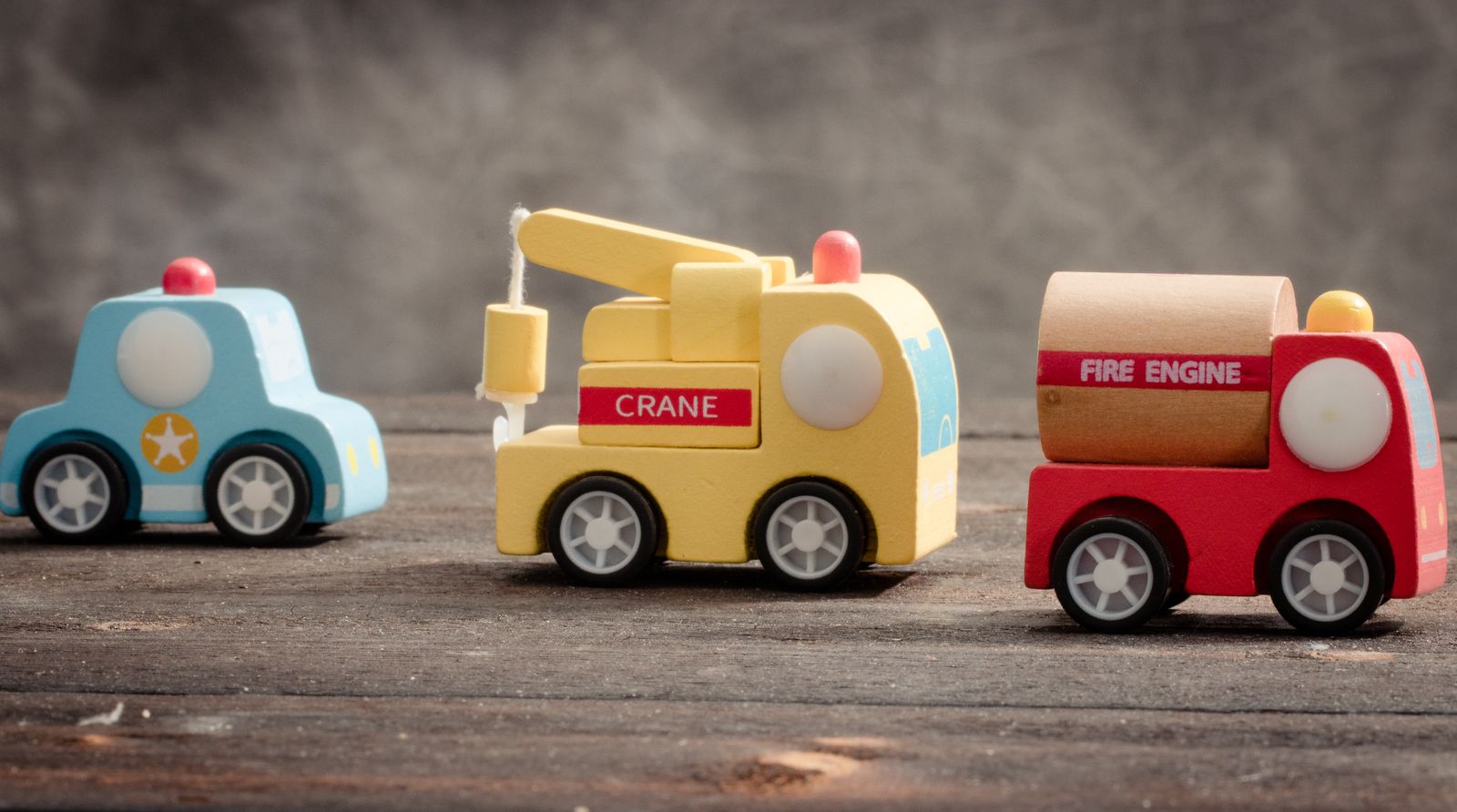 Three colorful wooden toy vehicles lined on a wooden table