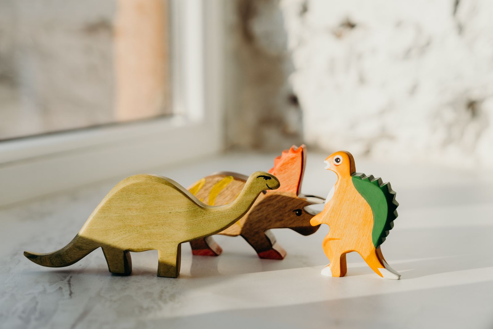 Painted wooden dinosaur toys arranged on a windowsill