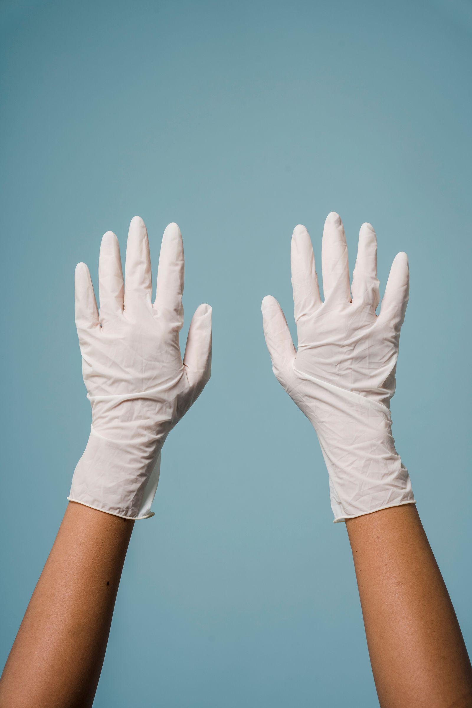 Pair of white latex medical gloves raised against blue