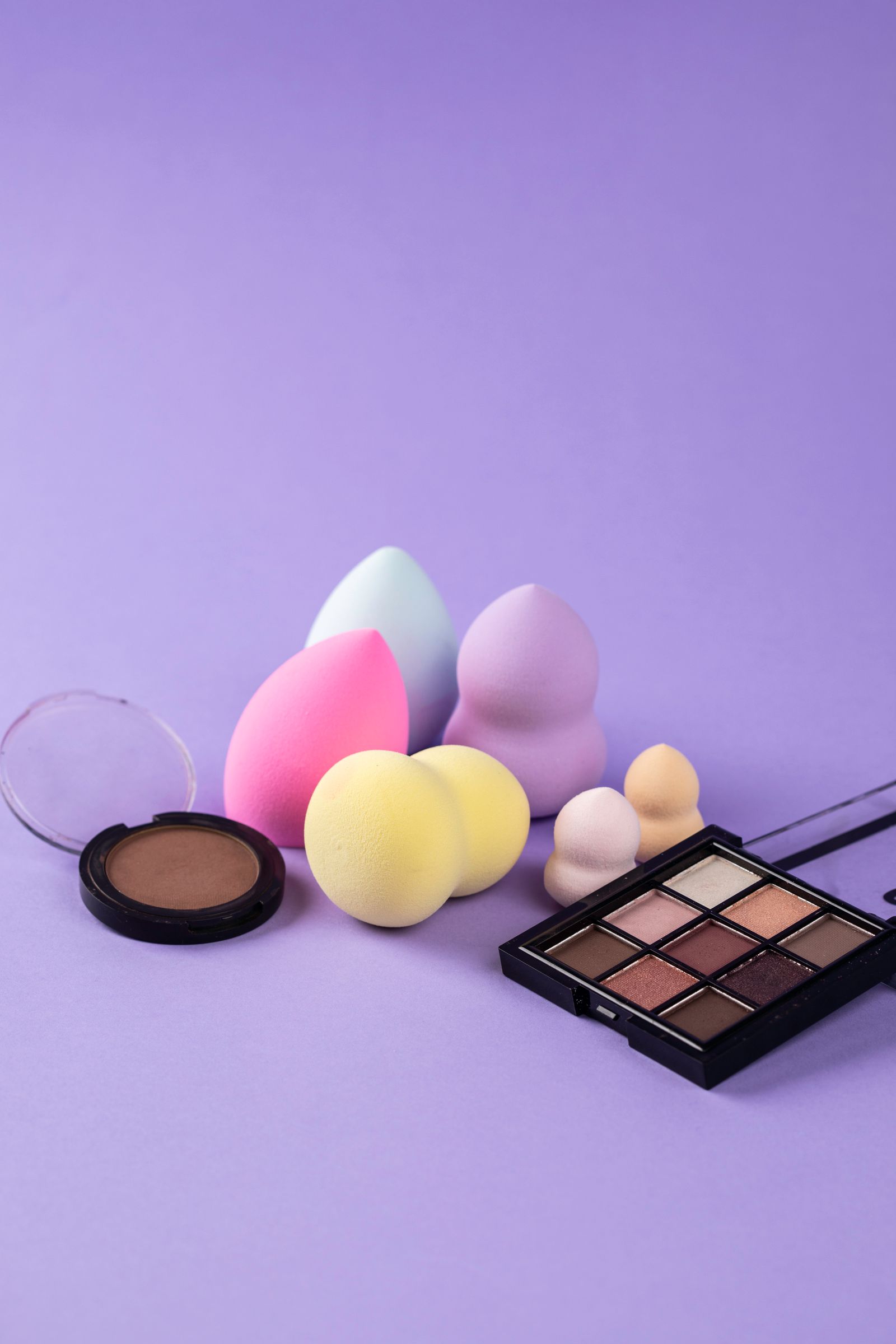 Colorful makeup sponges and eyeshadow palette on purple